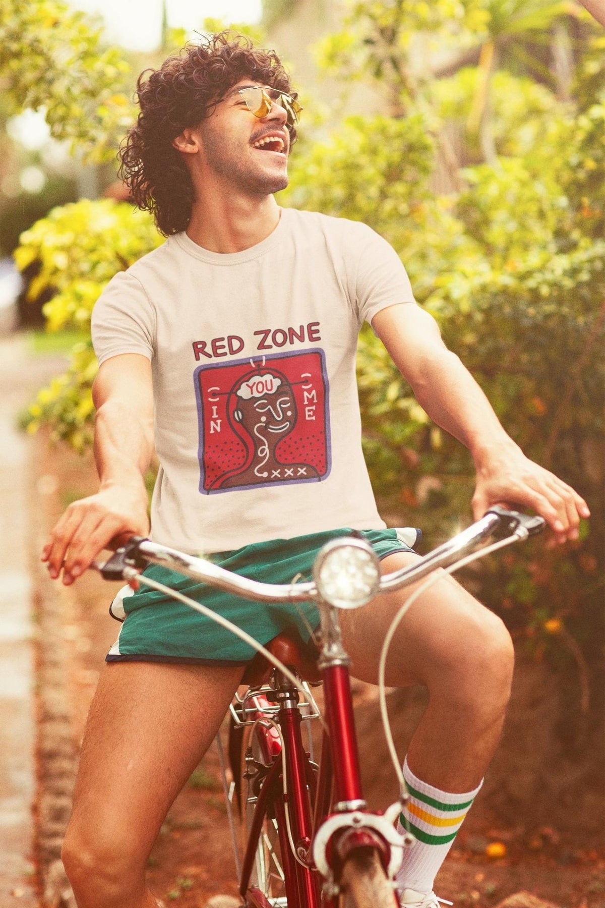 Man on bicycle wearing Barcelona grafic tee featuring Red Zone design with retro style, sunny outdoor setting.