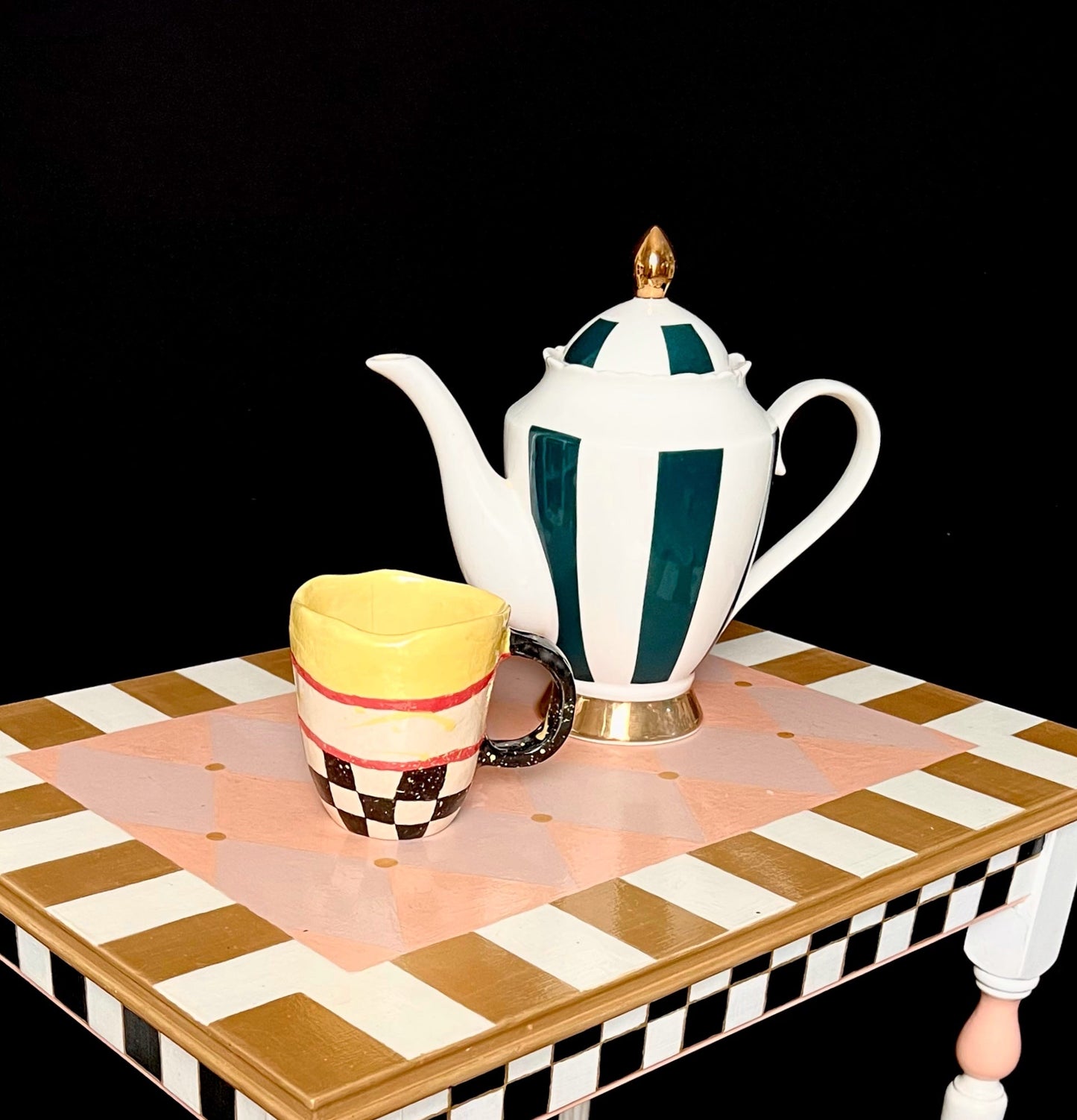 Mesita artesanal infantil con tetera blanca y azul, jarra amarilla y negra, mesa de diseño lúdico y geométrico.