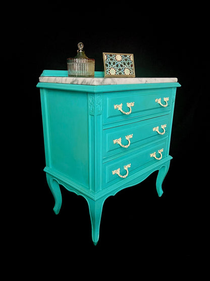 Mesita de noche artesanal en turquesa con tres cajones y superficie de mármol, diseño único y hecho a mano.